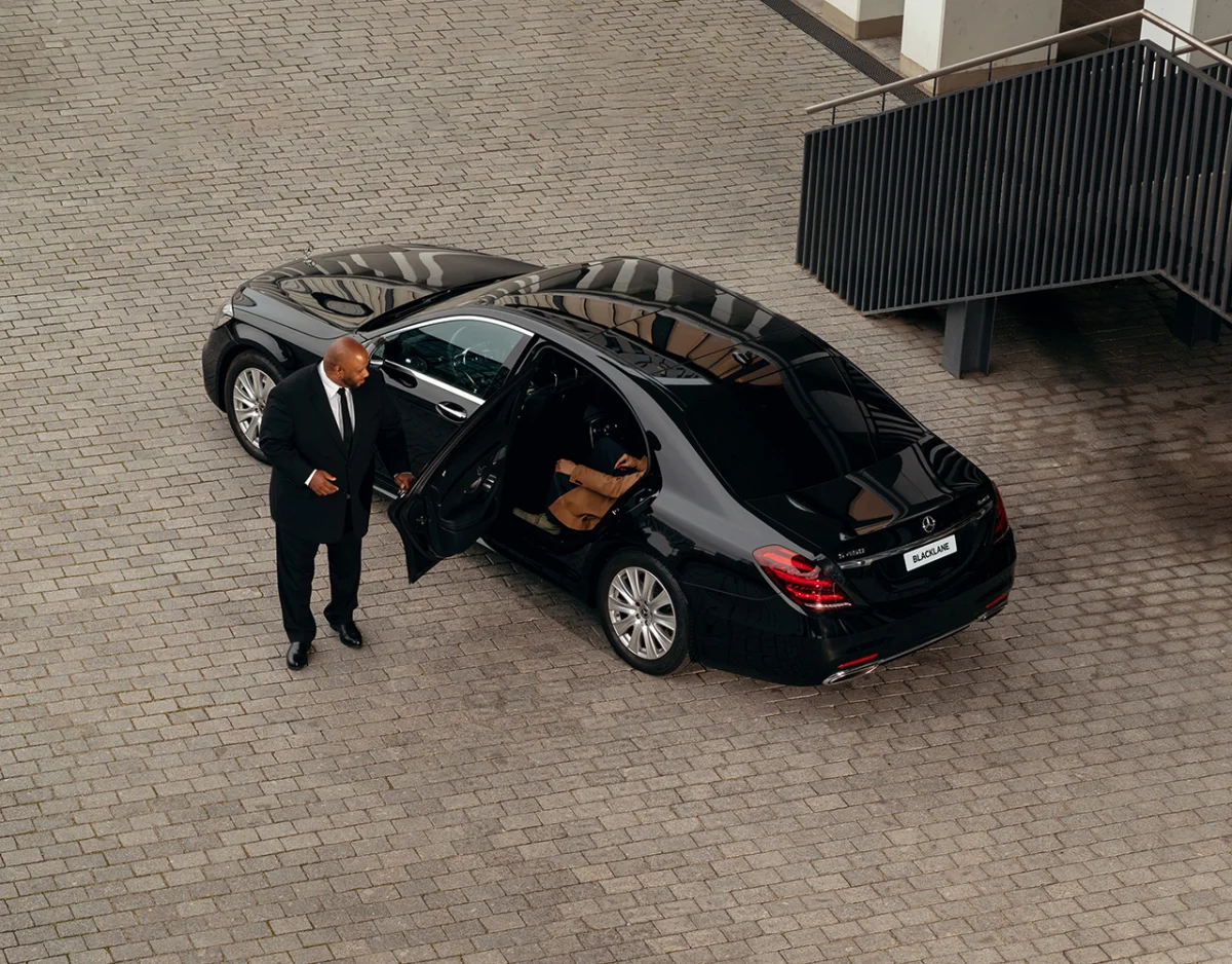 Chauffeur beside a black car at a villa entrance